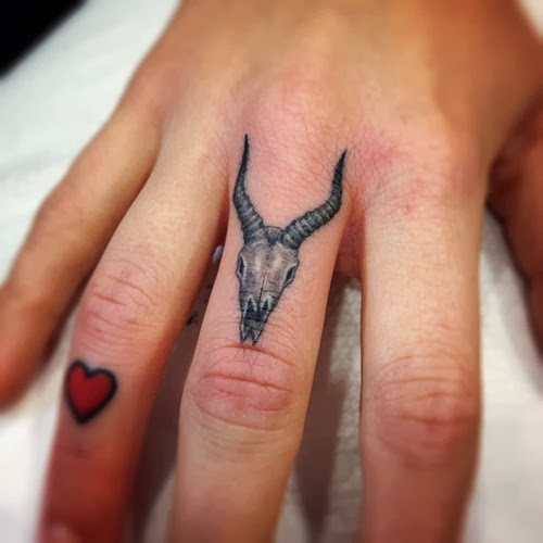 Women Finger Decorated With Aries Skull And Heart Tattoo Design